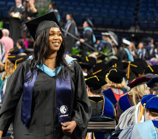 2024 Commencement image of a woman walking to the stage to receive her diploma with a smile