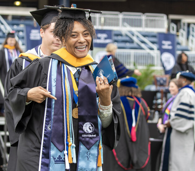 Athena Jones at Commencement with her diploma, excited and smiling at the camera while pointing to her oduglobal stole