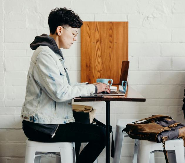 Student sits in a coffee shop on laptop while listening in to a lecture