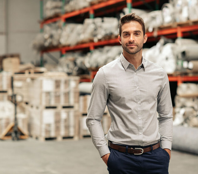 Man stands in a warehouse with his hands in his pockets and smiles