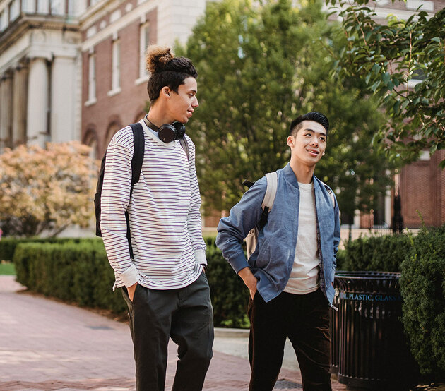 Two college students wearing backpacks have a conversation outside while walking to class.