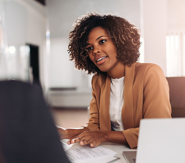 Two coworkers seated at a desk discuss education plans.