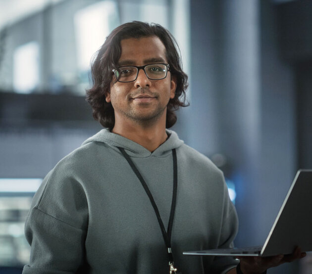 A programmer works at a laptop on a standing desk in a shared office space