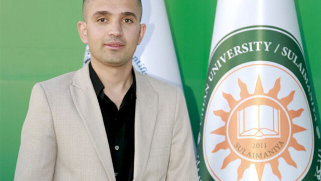 Photo of Sadiq Karim Omer standing next to a flag