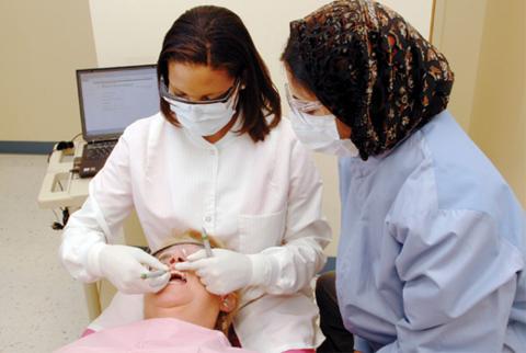 two dental hygienists working with patient in dental chair