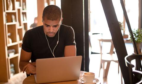 Man wearing earbuds and studying at laptop