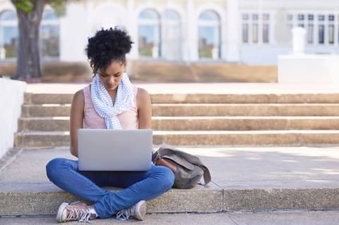 Young woman studying with laptop in front of academic building