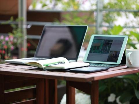 Two open laptops on a wooden desk with a paper notebook nearby