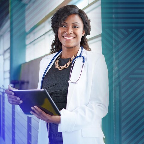 An African-American nurse smiles at the camera while holding an computer tablet.