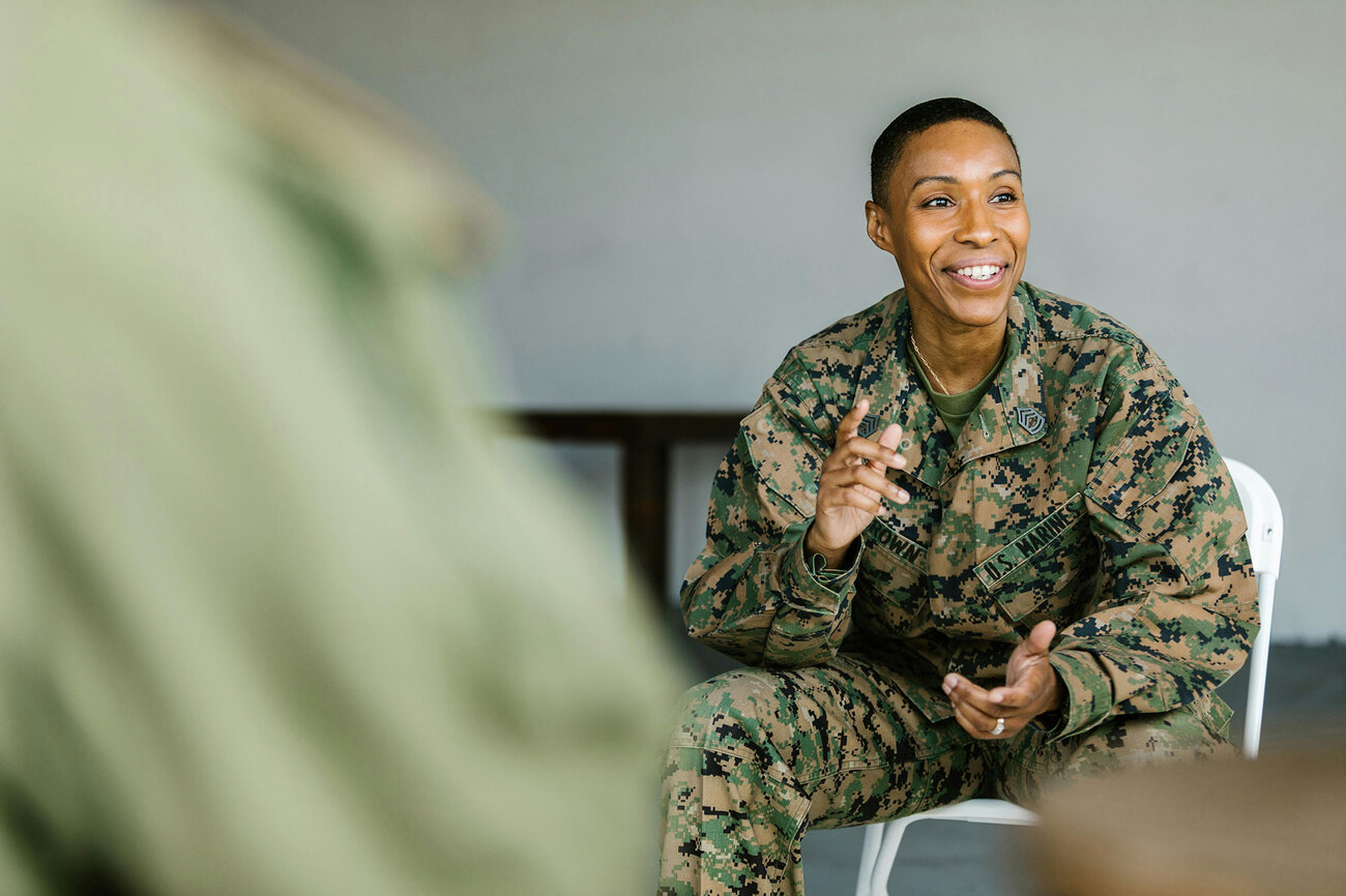 Military member sitting and talking to a group. She is smiling.