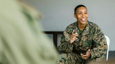 Military member sitting and talking to a group. She is smiling.