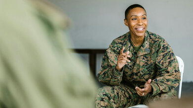 Military member sitting and talking to a group. She is smiling.