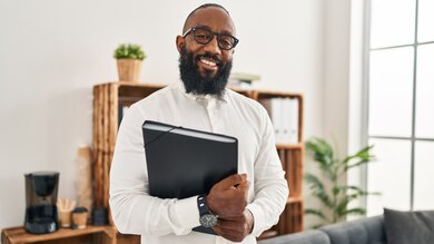 African American man holding a binder and smiling confidently in his office.