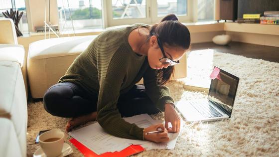 Woman sitting on floor with laptop and study notes