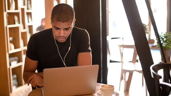 Man wearing earbuds and studying at laptop