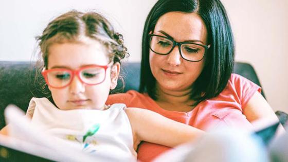 Child sitting on woman's lap and reading a book