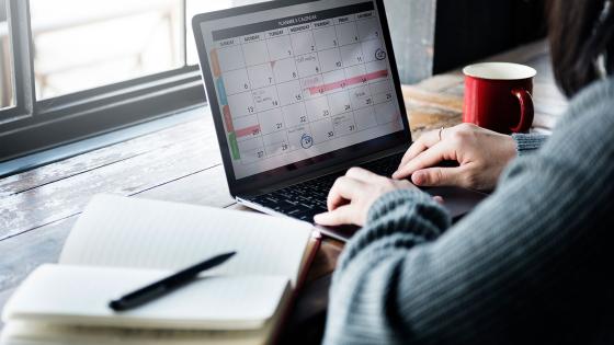 Person sitting at computer organizing a calendar with a journal nearby