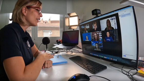 A woman seated at a computer is interacting with a screen of online meeting attendees