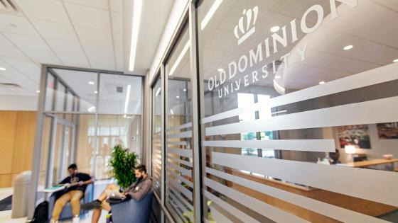 Old Dominion University logo on a glass window, with students seated and studying in the background.