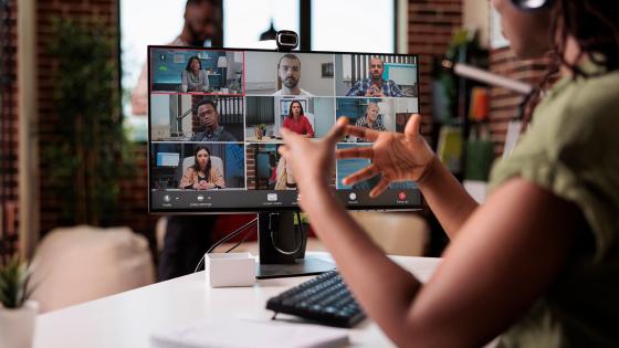 A woman seated at a computer gestures with her hands as she talks to classmates online