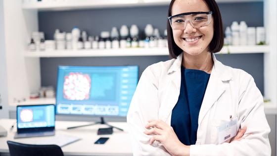 A clinical laboratory specialist stands confidently in front of a computer for health research.