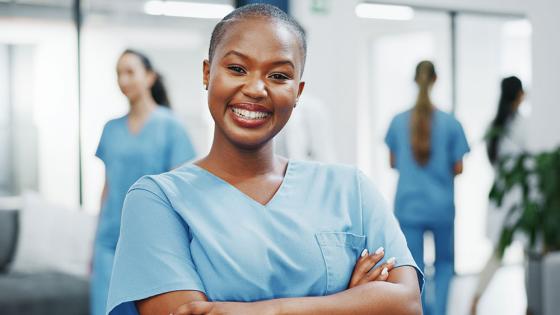 A nurse smiles confidently at the camera in the hallway of a busy medical clinic.