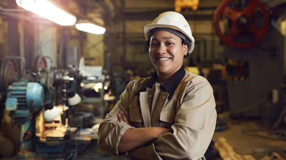 Smiling person wearing a white helmet, standing in a workshop