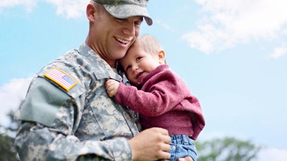 Military service member holds his child while in uniform