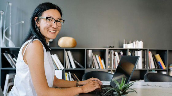 A smiling business women is seated at an office table with a laptop