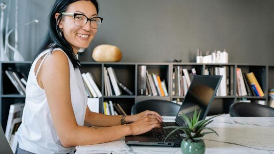 A smiling business women is seated at an office table with a laptop