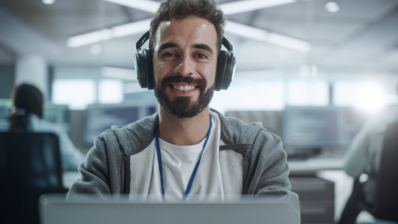 Student sits at his computer in a shared office space smiling at the camera