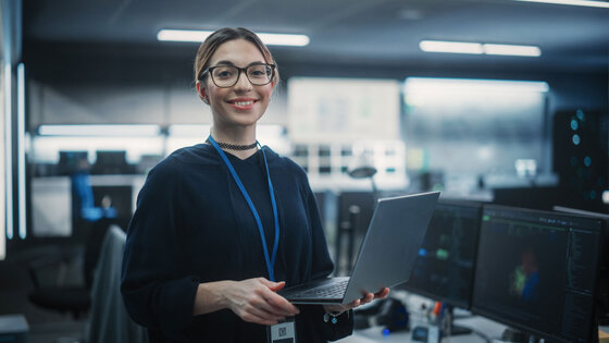 Woman stands holding a laptop in a workspace with servers