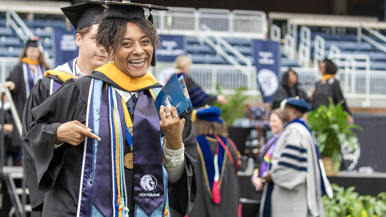Athena Jones at Commencement with her diploma, excited and smiling at the camera while pointing to her oduglobal stole