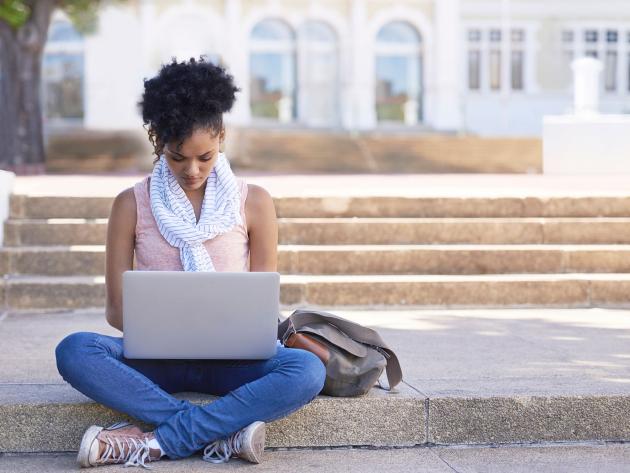 Young woman studying with laptop in front of academic building