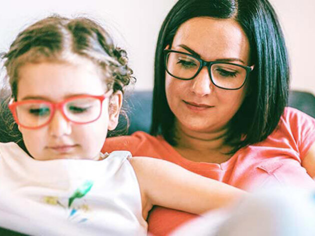 Child sitting on woman's lap and reading a book