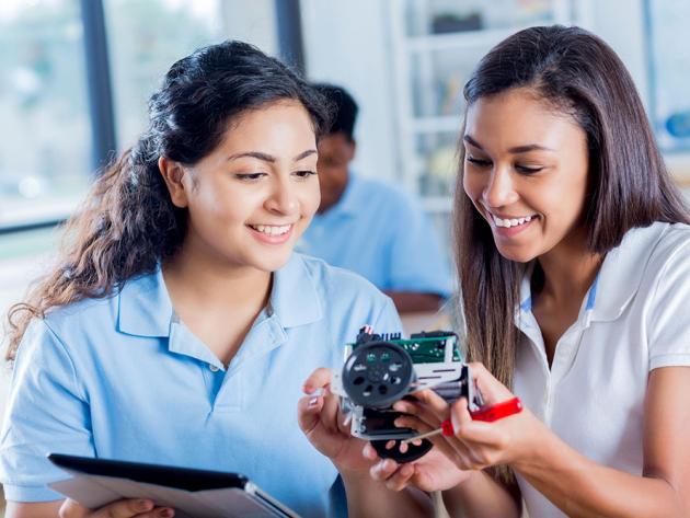 Two smiling female high school students examine a robotic component