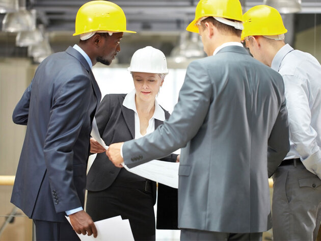 Engineering management staff gather around a large print out in a warehouse setting.