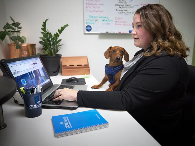 Woman works on her computer with a little dog nearby as she finishes college online