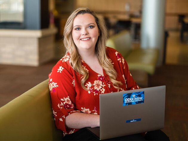 A smiling female ODU student seated on a padded bench with an ODU laptop computer open on her lap.