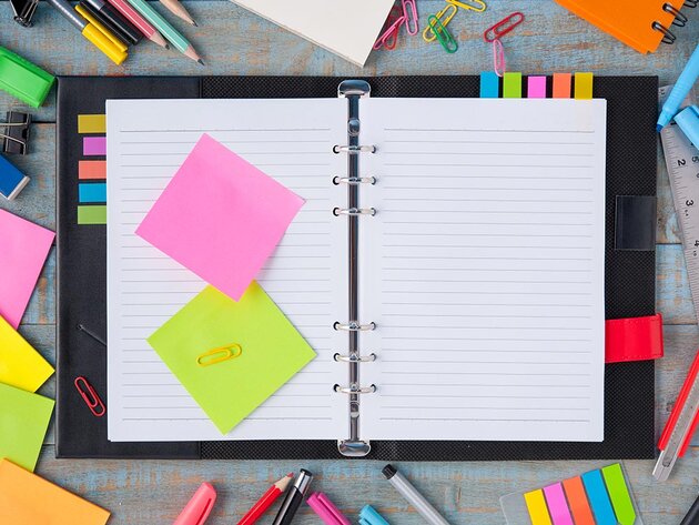 Overhead view of an open notebook with sticky notes, pens, and paperclips scattered around it on the table.