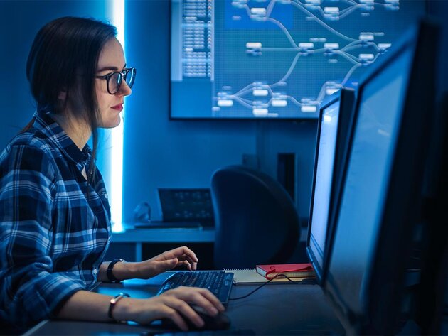 A female professional in the cybersecurity field works at a computer on a desk with dual monitors.