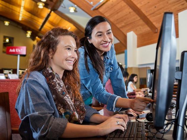 A female librarian guides a young student to find information at a desktop computer.