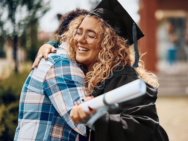 Happy college graduate hugs a family member outside on a sunny day.