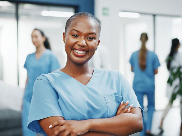 A nurse smiles confidently at the camera in the hallway of a busy medical clinic.