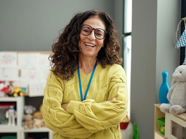 An early education teacher laughs happily in her classroom surrounded by bookshelves and toys.