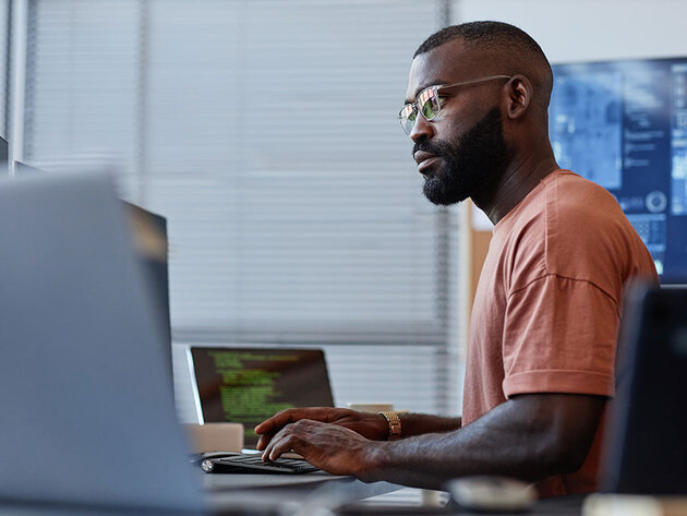 A data professional works at a desk with multiple computer monitors displaying different information.