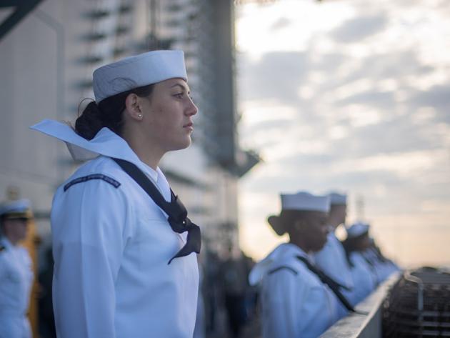 Enlisted Navy personnel stand at attention on the deck of a ship at sea.