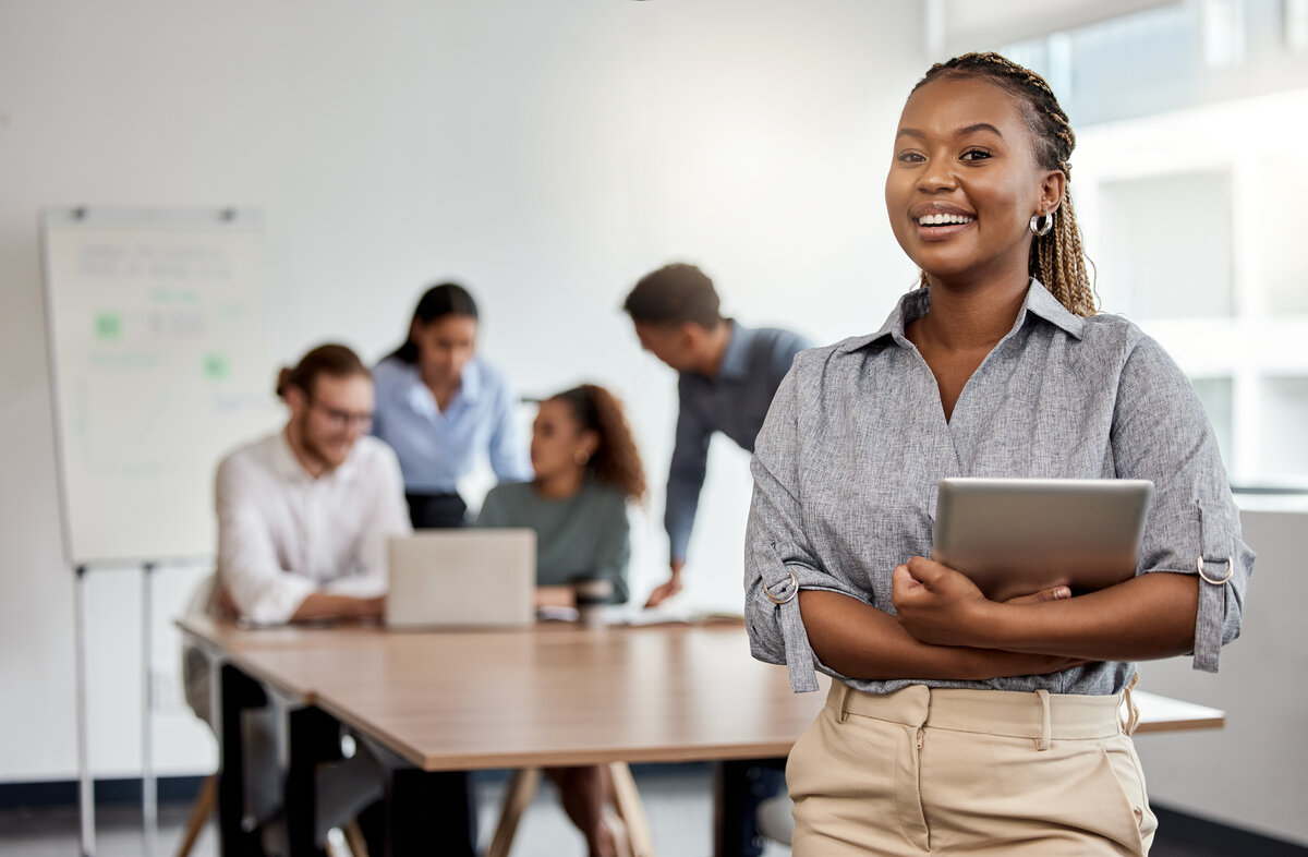 Woman with tablet in a boardroom with colleagues meeting behind her 