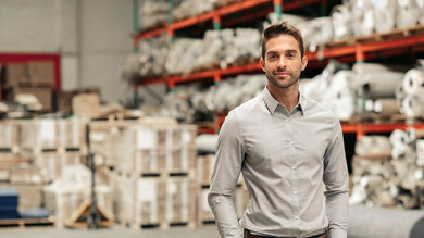 Man stands in a warehouse with his hands in his pockets and smiles