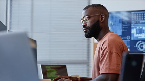 A data professional works at a desk with multiple computer monitors displaying different information.